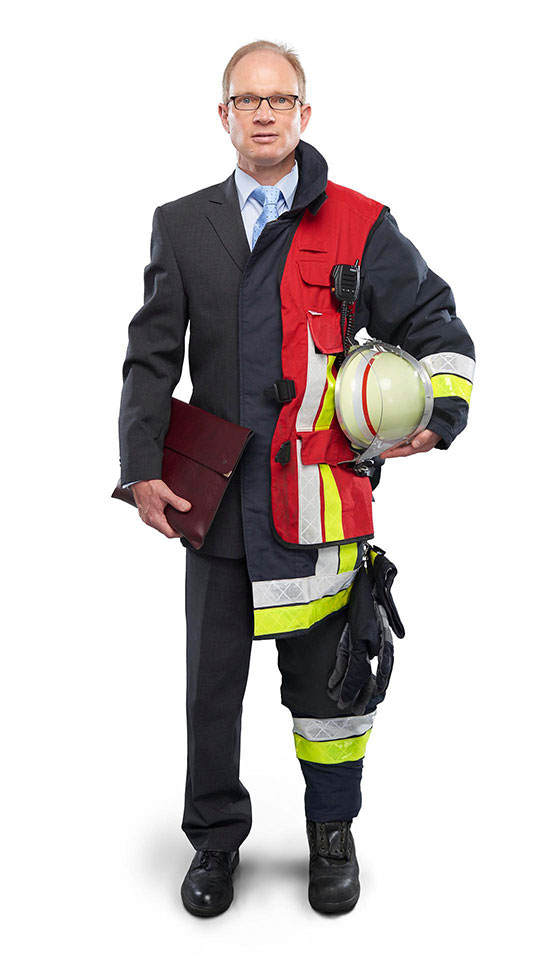 Fotomontage eines Mannes: Zur einen Hälfte im Businessanzug, zur anderen Feuerwehrmann in Uniform. Er hält eine Ledermappe und einen Feuerwehrhelm in den Händen.
