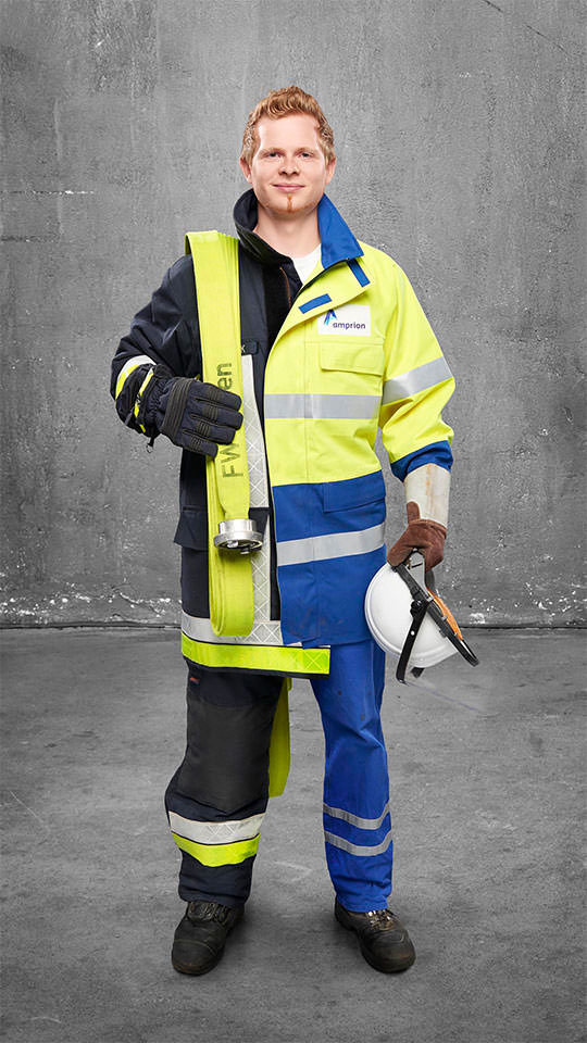 Fotomontage eines Mannes: Halb Hochspannungselektroniker in gelb-blauer Arbeitskleidung, halb Feuerwehrmann in Uniform. Er trägt einen Feuerwehrschlauch über der Schulter.