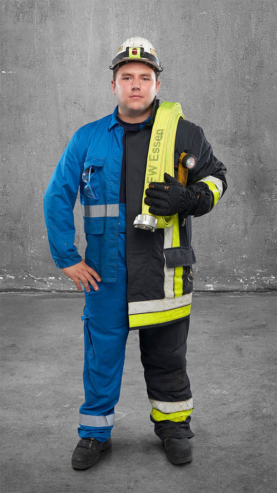 Fotomontage eines Mannes: Halb Kraftwerker in hellblauer Arbeitskleidung, halb Feuerwehrmann in Uniform. Er trägt einen Feuerwehrschlauch über der Schulter.